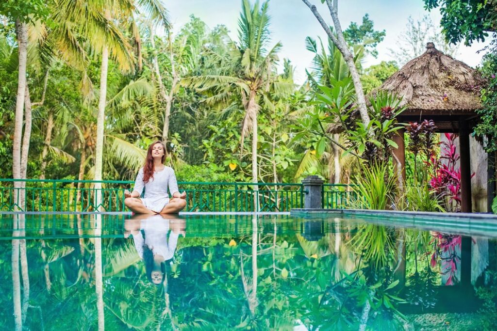 Woman meditating by tropical pool in nature