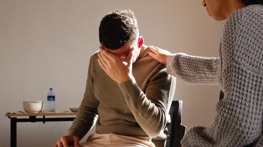 Man covering face while receiving support