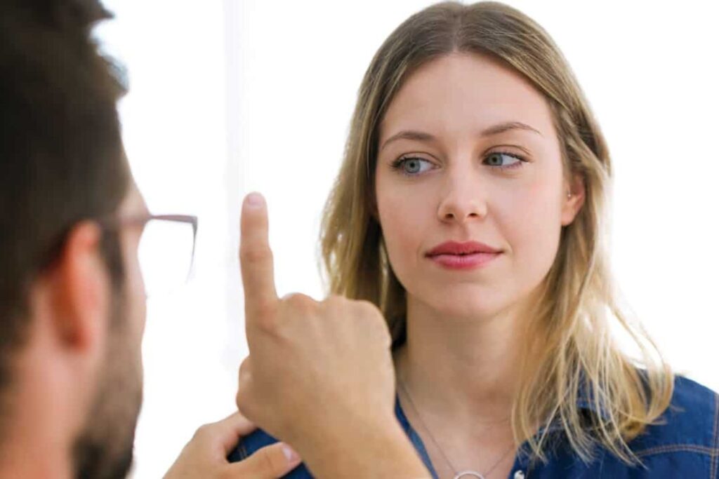 Close-up of a woman looking at a person in front of her who is holding up one finger, possibly giving instructions or guiding a focus exercise.