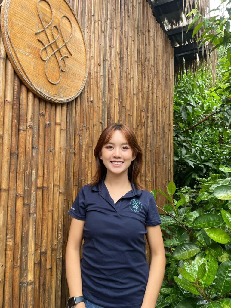 Smiling woman standing by bamboo wall and greenery